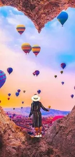 A woman gazing at colorful hot air balloons through a heart-shaped rock opening.