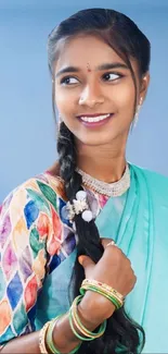 Woman in colorful Indian attire smiling against a sky blue background.