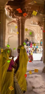 Two women in traditional attire amidst colorful confetti in an Indian palace.