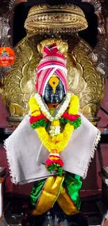 Golden deity idol adorned with vibrant garlands and traditional attire.