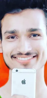 Smiling individual holding iPhone against vibrant orange background.