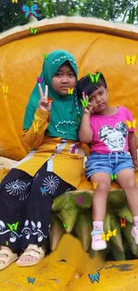 Two kids sitting surrounded by colorful butterflies on a bright yellow seat.