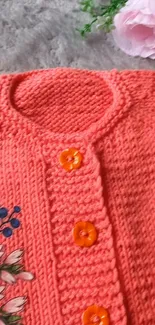 Coral knitted sweater with floral design and orange buttons.