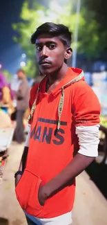 Young man in a red hoodie on a vibrant city street at night.