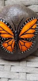 Orange monarch butterfly painted on a rock with a woven background texture.