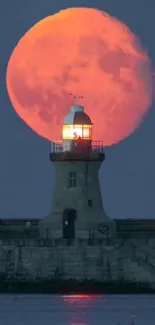 Orange moon rising behind a lighthouse at night.