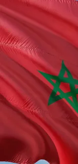 Red Moroccan flag with green star, waving in bright blue sky.