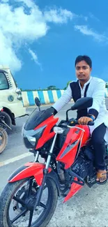 Man riding a red motorcycle under a bright blue sky with clouds.