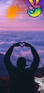 Silhouette with heart hands and peace sign over a vibrant mountain landscape.