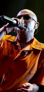 Performer holding a microphone on stage, wearing an orange shirt.