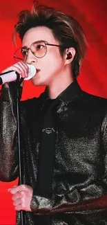 Singer performing on stage with red background.