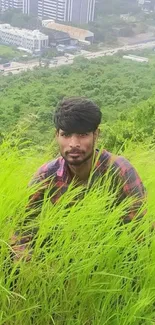 Person sitting in lush green grass with city in the background.