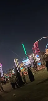 Night view of an amusement park with glowing neon lights and vibrant activity.