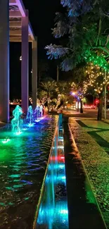 Illuminated night fountain with vibrant colors and trees.