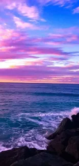 Vibrant sunset over ocean with pink and purple sky and crashing waves on rocks.