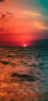 Vibrant sunset over ocean with red and teal hues, capturing serene waves.