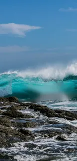 Vivid blue ocean wave crashing on rocks with a clear sky.