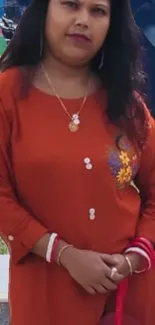 Woman in orange dress with floral embroidery, standing outdoors.