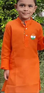 Child in vibrant orange traditional attire holding a flag with greenery background.