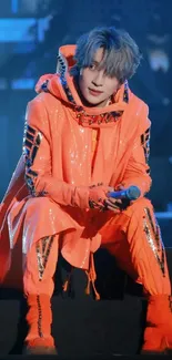 A performer in vibrant orange on stage with dynamic lighting.