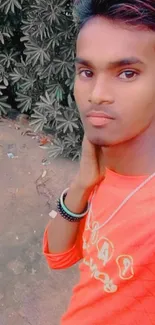 Young man in vibrant orange shirt with natural leafy background.