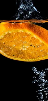 Orange slice splashes in black water, creating bubbles.