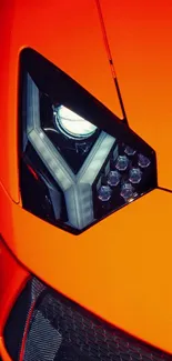 Close-up of vibrant orange sports car headlight.