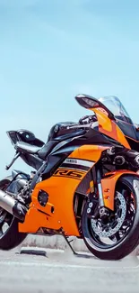 Orange sports motorcycle set against a bright blue sky.