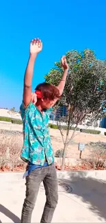 Young man dancing outdoors under a vibrant blue sky.