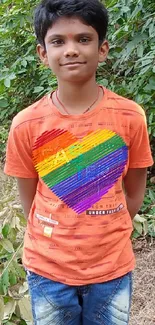 Young child standing in nature wearing an orange shirt with a colorful heart design.