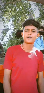 Young person in red shirt under a tree.