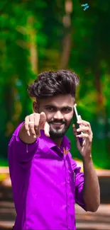 Man in purple shirt points, holding phone outdoors.