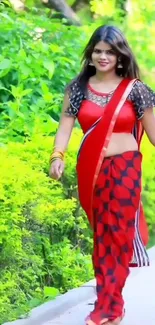 Woman in red saree walking outdoors with green background.