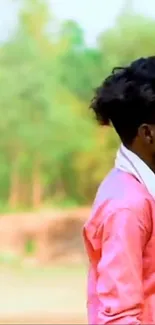 Man in pink shirt outdoors with lush green backdrop.