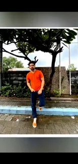 Man in orange shirt outdoors with urban backdrop.