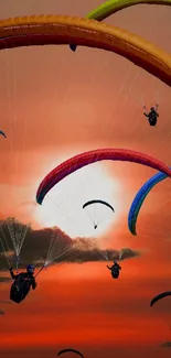 Colorful paragliders soar at sunset over a vibrant orange sky.