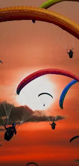 Colorful paraglider silhouettes against an orange sunset sky.