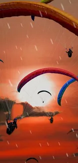 Colorful paragliders soar against a vibrant orange sunset sky.