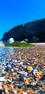 Pebble beach with blue sky and ocean waves, perfect mobile wallpaper.