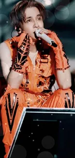 Performer in vibrant orange attire on stage during concert.