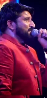 Performer singing passionately in a vibrant red jacket on stage.