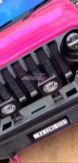 Front view of a vibrant pink Jeep vehicle, showcasing its rugged grille design.