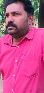 Person in vibrant pink shirt outdoors with green background.