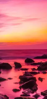 Vibrant pink sunset over ocean with rocks in foreground.