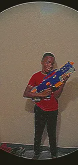 Young boy with toy blaster on playful wallpaper.