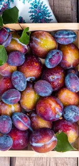 Vibrant plums in a wooden crate with leaves on a rustic table.