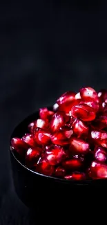 Close-up of vibrant crimson red pomegranate seeds in a black bowl.