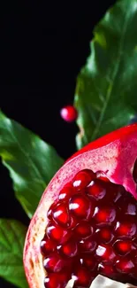 Vibrant pomegranate with red seeds and green leaves on black background.