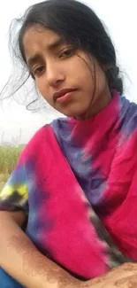 Woman in colorful shawl sitting outdoors.