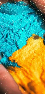 Vibrant blue and orange powder with sparkles on a mobile wallpaper.